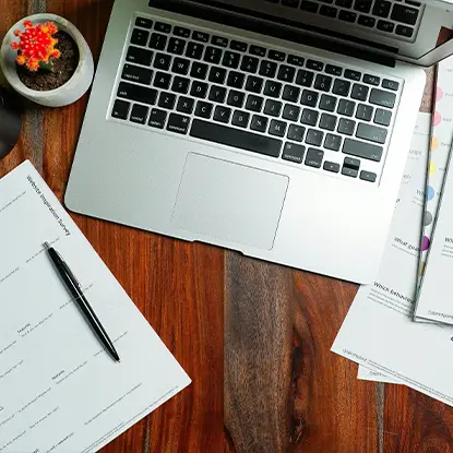 A stack of paper invoices beside a laptop on an office desk